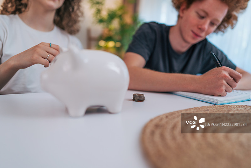 青少年使用储蓄罐和笔记本管理财务图片素材