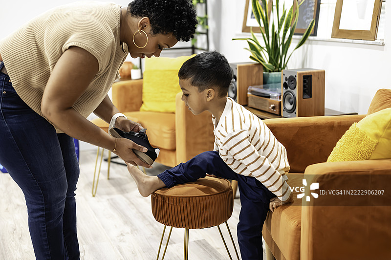 非裔美国母亲在家里给她的多种族儿子穿鞋，展现生活中的育儿片段图片素材