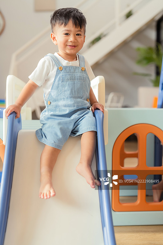 亚洲幼儿男孩在家中的游乐屋隧道和滑梯上爬行，快乐地玩耍，享受与塑料玩具的乐趣，展现出健康的生活方式。图片素材