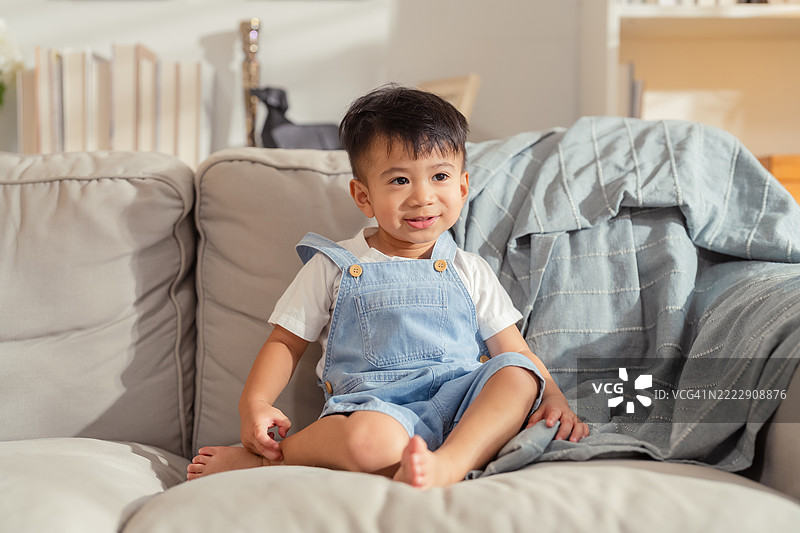 可爱好奇顽皮的亚洲幼儿（18-23个月）坐着放松，微笑着，展现出愉快美好的家庭生活理念。图片素材