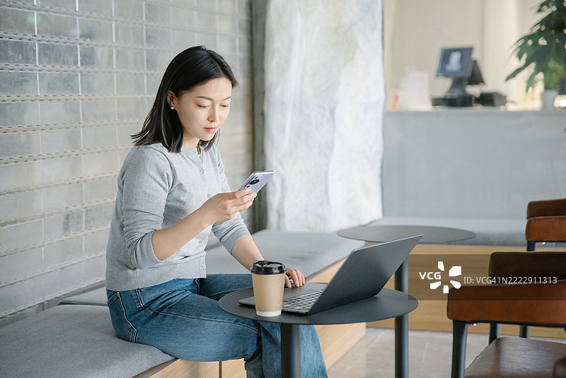 一位亚洲女性在咖啡店用手机浏览网页图片素材