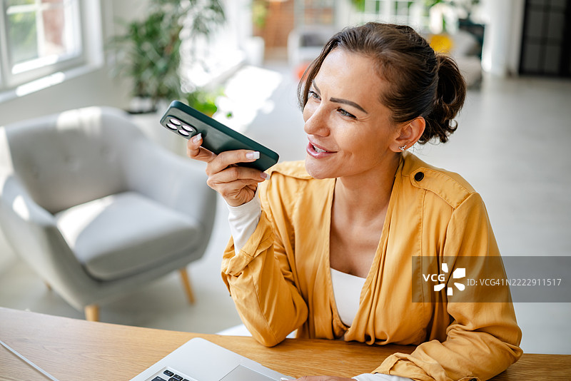 女性在明亮现代的房间里坐在桌子旁进行视频通话，正值白天。图片素材