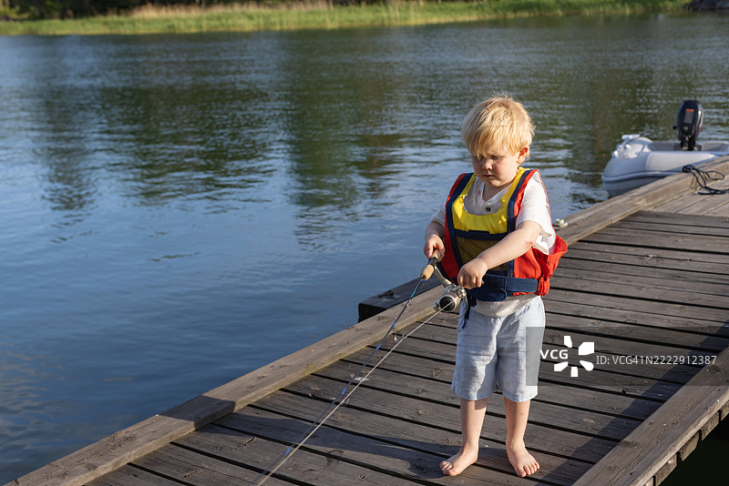 年轻男孩在风景如画的湖边木栈道上钓鱼图片素材