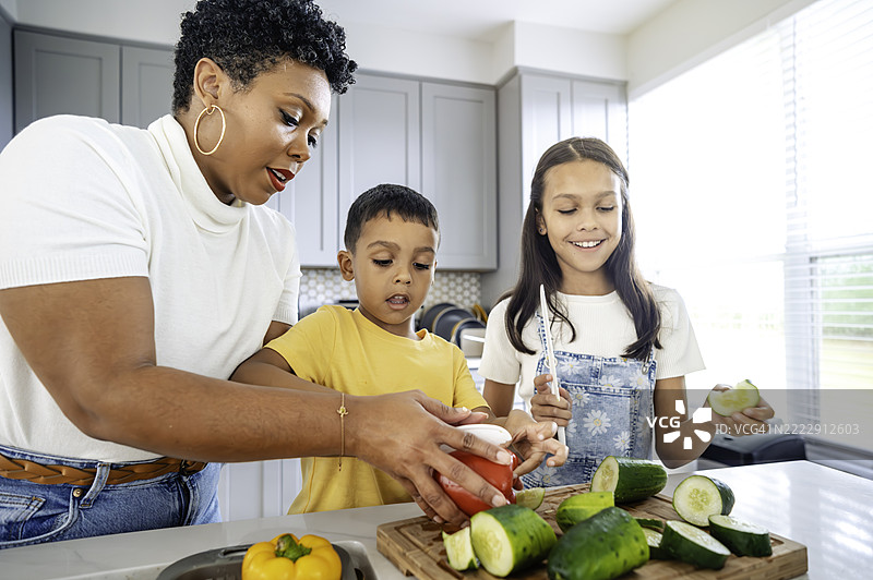 两个多种族的孩子在厨房与妈妈一起准备健康餐，BIPOC家庭团聚。图片素材