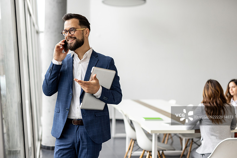商人在办公室里一边打电话一边拿着笔记本电脑图片素材