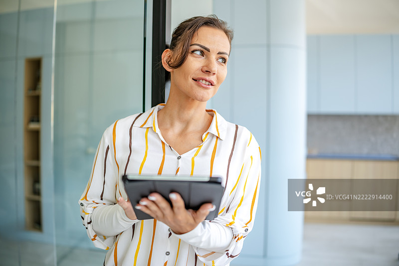 自信的女性穿着条纹衬衫，在现代办公室环境中白天使用平板电脑图片素材