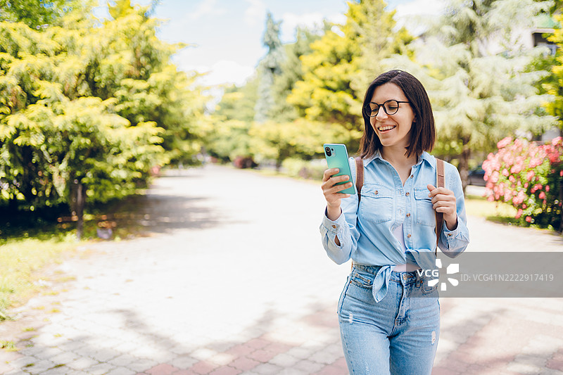 年轻女性一边走路一边使用手机，享受其中。图片素材
