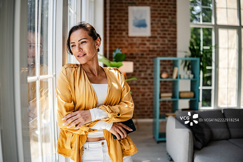 沉思的女性在现代客厅中凝视窗外，阳光透过窗户洒入，装饰风格时尚。图片素材