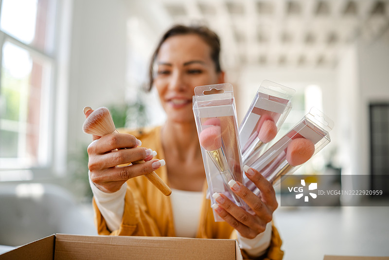 女人在明亮的室内空间中拆箱化妆刷，微笑着享受她的新美容产品图片素材