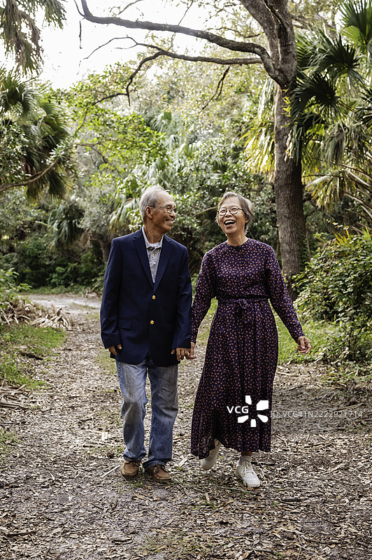 成熟的华裔老年夫妇在户外自然中手牵手散步，充满爱意。图片素材
