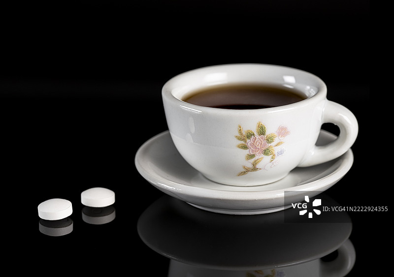 黑色背景上的咖啡杯和两片阿司匹林。图片素材