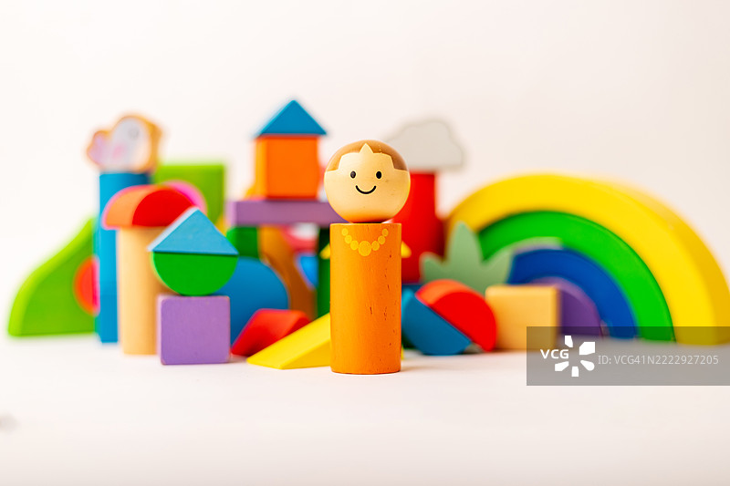 微笑的木制玩具人站在五彩缤纷的积木前，象征着童年和创造力。图片素材