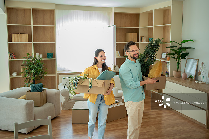 快乐的情侣搬着箱子和植物进入新家图片素材