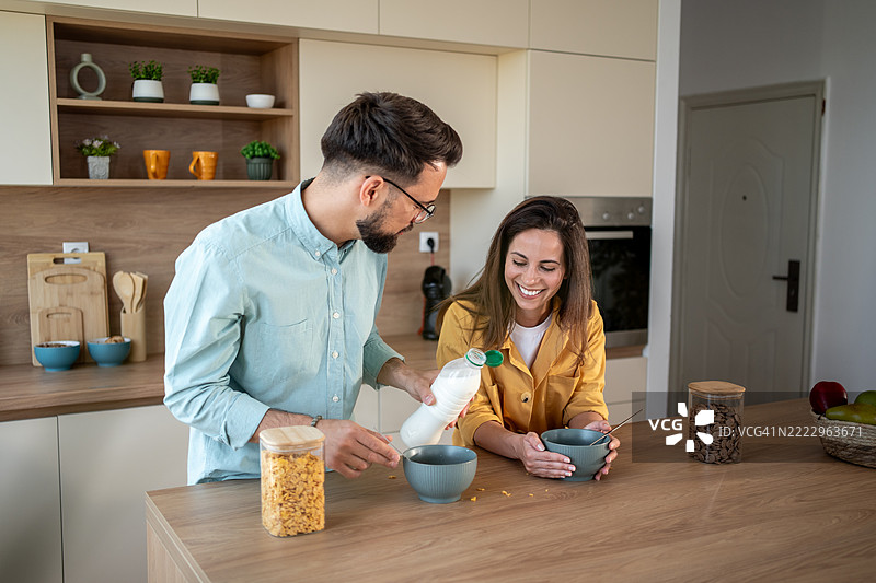 快乐的情侣在厨房岛上准备牛奶和谷物早餐图片素材