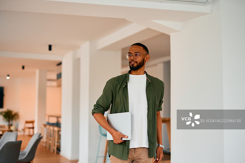自信的年轻经理走在现代办公室里，手里拿着笔记本电脑图片素材