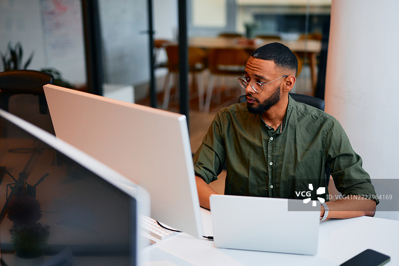 专注的年轻程序员在现代办公室中使用多台设备工作图片素材
