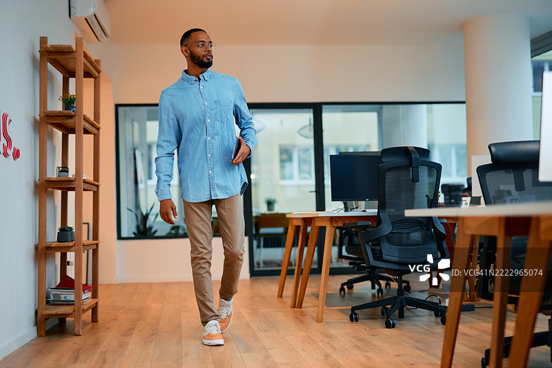 自信的年轻经理手持平板电脑走过办公室图片素材