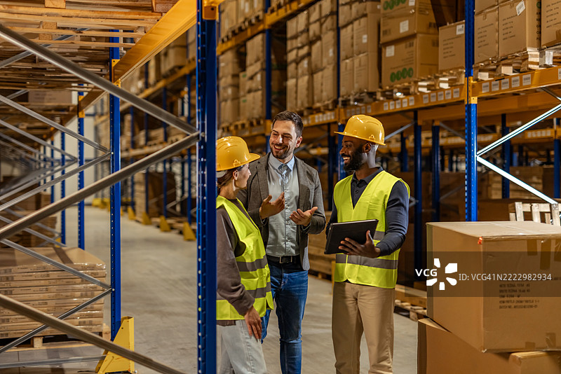 团队在货架和箱子环绕的仓库过道中讨论运营图片素材