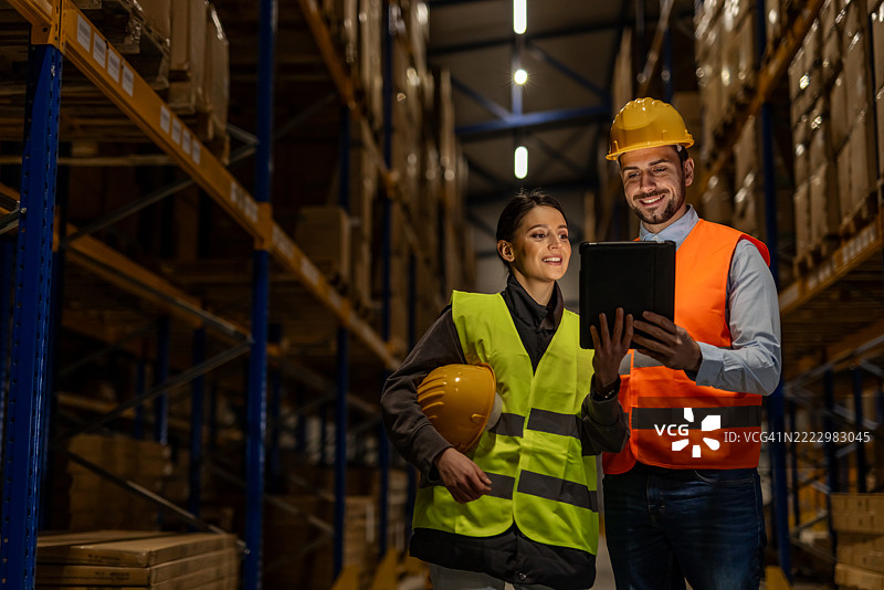 仓库工人使用数字技术和个人防护装备协作进行库存管理图片素材