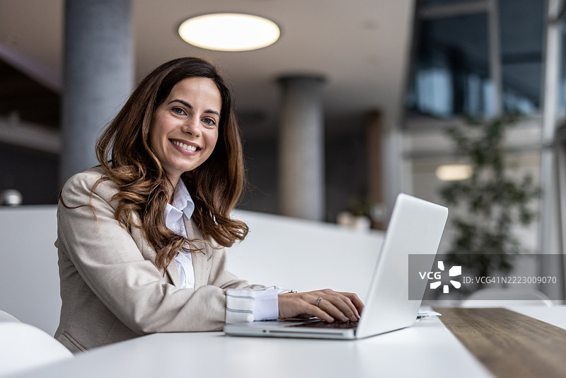 微笑的女商人在现代办公室里使用笔记本电脑工作图片素材