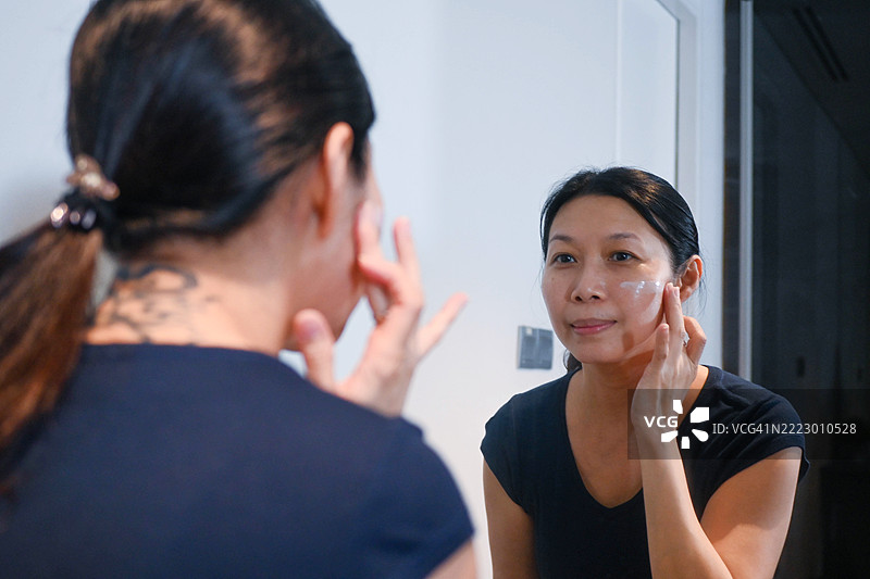 一位亚洲女性在镜子前仔细涂抹面膜的特写镜头图片素材