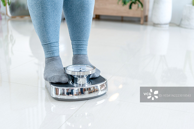 脚踩在秤上。减肥和饮食概念。女性在称重。健身女士在节食。减肥和营养学。黑暗的深夜氛围。图片素材