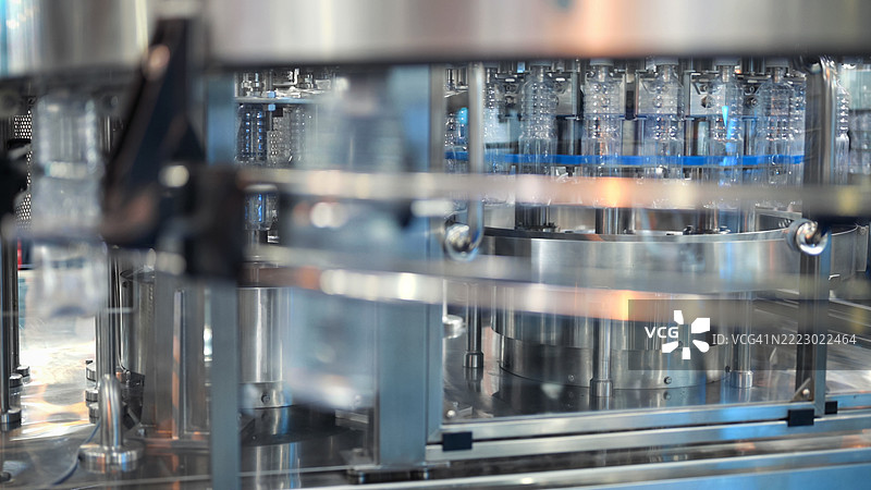 高精度灌装设备，配有透明液体容器，高容量瓶装和封口机，工业自动化生产线中的同步多步骤包装系统图片素材