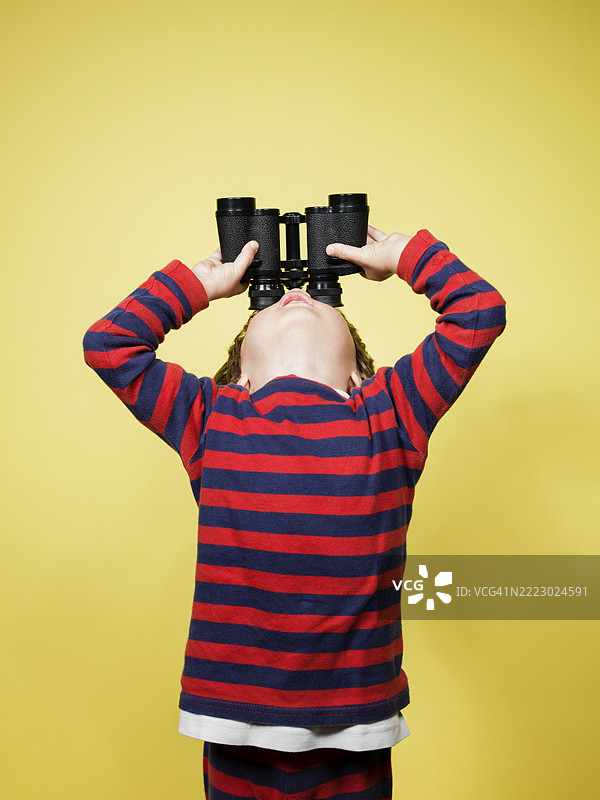 穿着条纹睡衣的孩子好奇地通过望远镜观察图片素材