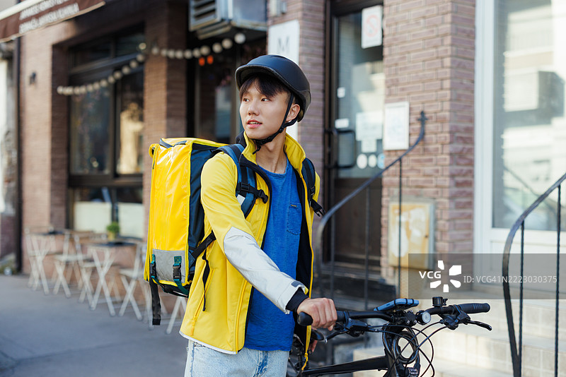 年轻的快递员在城市中，背着黄色背包，戴着头盔图片素材