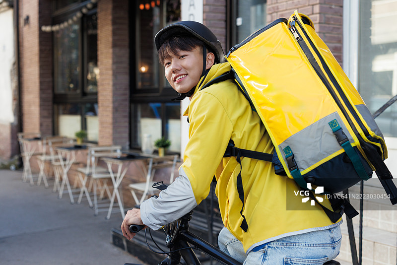 年轻的快递员在城市环境中背着黄色背包图片素材