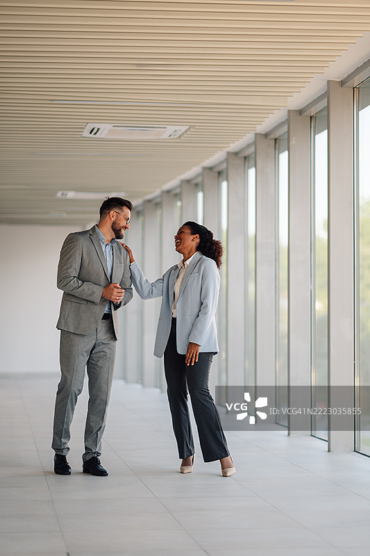 女商人在办公室走廊与男商人聊天时轻触他的肩膀图片素材
