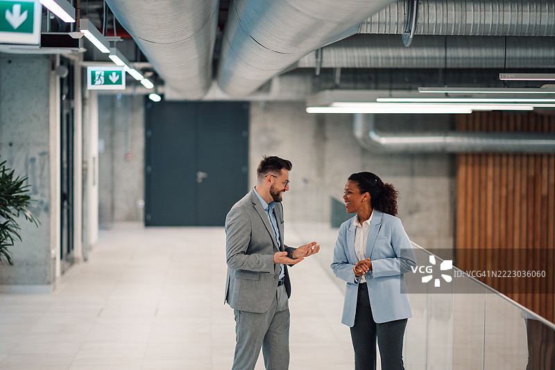商务人士在现代办公室走廊交谈并微笑图片素材