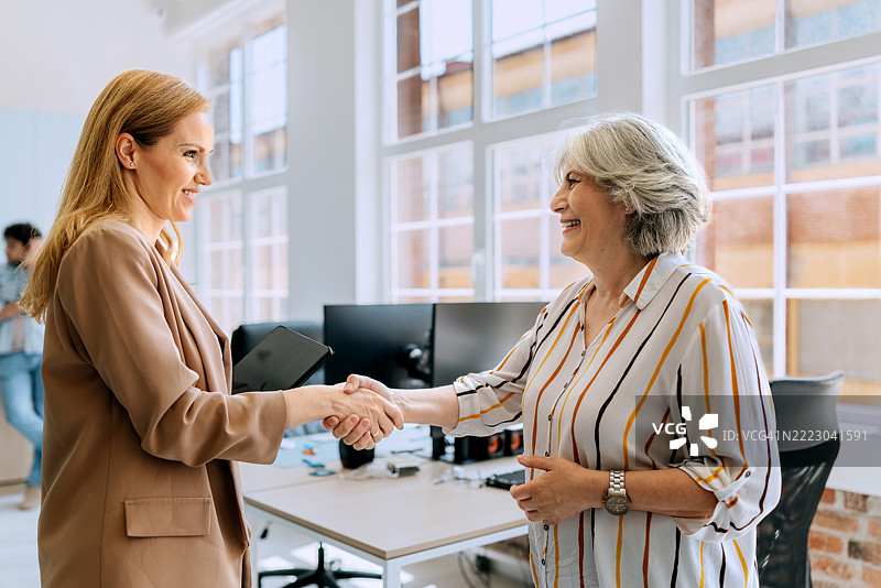 两位成熟的女性同事在现代办公室握手图片素材