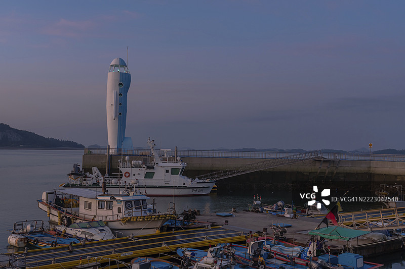 韩国务安郡。2020年9月27日：停靠在浮动码头的船只，背景是务安海滩的飞机形灯塔。图片素材