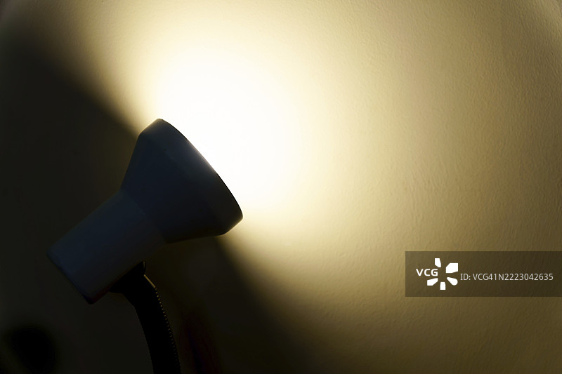 桌灯发出的光束照亮墙壁，营造出温暖的光线和阴影。图片素材