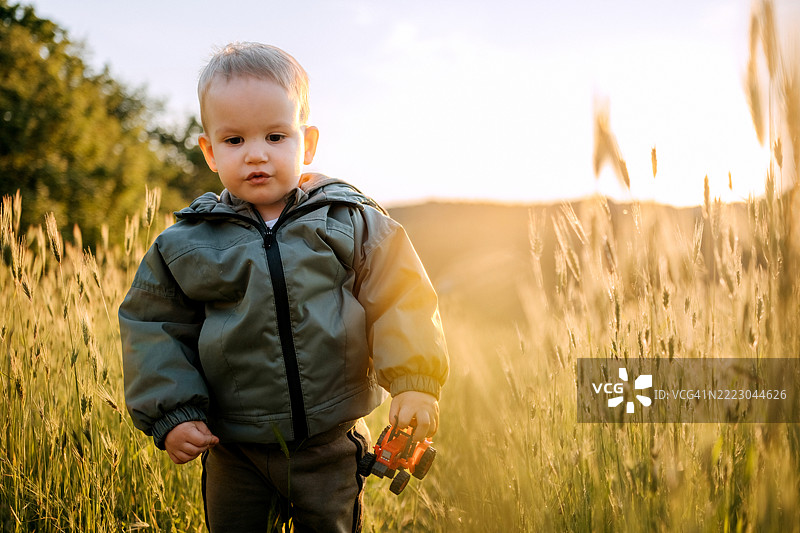 可爱的小男孩在日落时分的草地上走着图片素材
