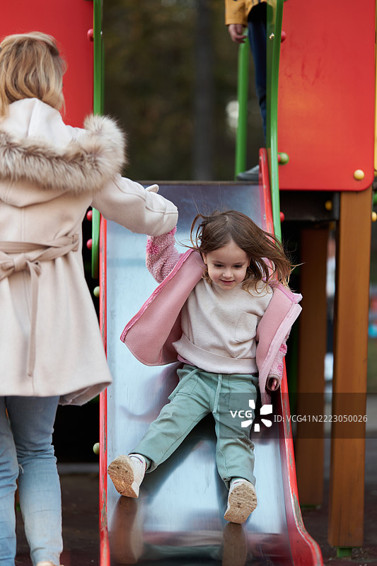 小女孩正在滑滑梯，她的妈妈握着她的手。图片素材