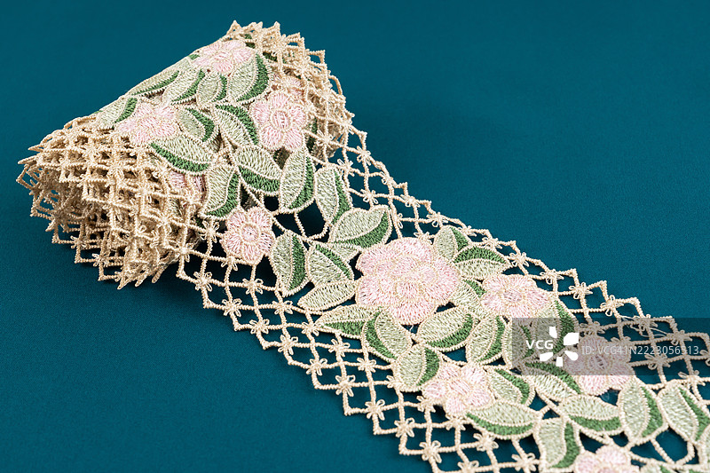 花朵和绿叶蕾丝纺织品卷在绿色布料背景上。图片素材
