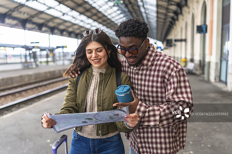 年轻的多民族情侣在火车站站台上研究地图，规划着他们假期的下一个目的地。图片素材