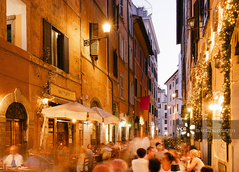 人们在繁忙的罗马街道上黄昏时分的餐厅和酒吧外用餐图片素材