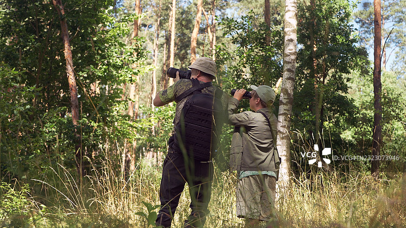 父子在夏季的树林和草地中一起。鸟类观察家庭冒险。通过望远镜观察和拍照。鸟类观察。图片素材