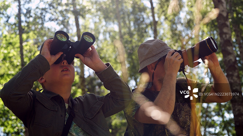 父子在树木繁茂的森林中。鸟类观察家庭冒险。通过望远镜观察和拍照。鸟类观察。图片素材