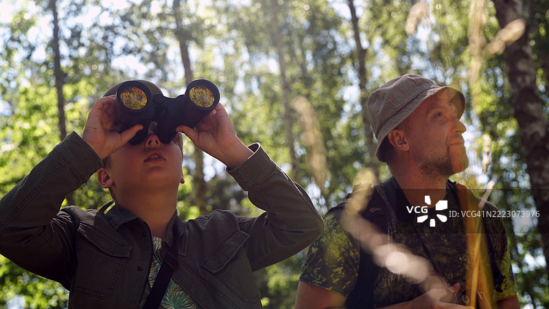 父亲和儿子在绿色的夏季森林中共度时光。家庭鸟类观察冒险。通过望远镜观察鸟类。图片素材