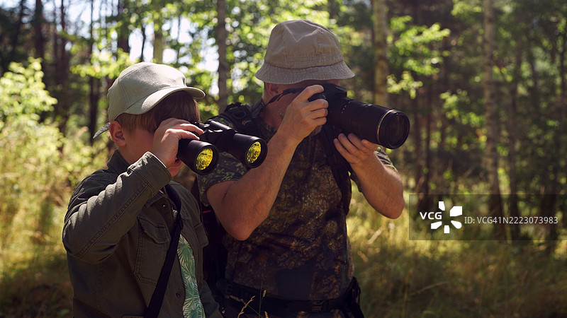 父亲和儿子在绿色的夏季森林中共度时光。鸟类观察家庭冒险。使用望远镜和拍照。观鸟活动。图片素材