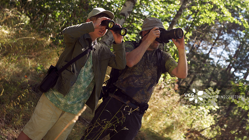 父亲和儿子在绿树成荫的森林中共度时光。鸟类观察家庭冒险。使用望远镜和拍照。观鸟活动。图片素材