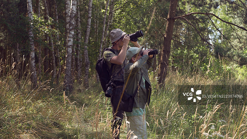 父亲和儿子在郁郁葱葱的树林中共度时光。家庭鸟类观察冒险。鸟类观察。图片素材