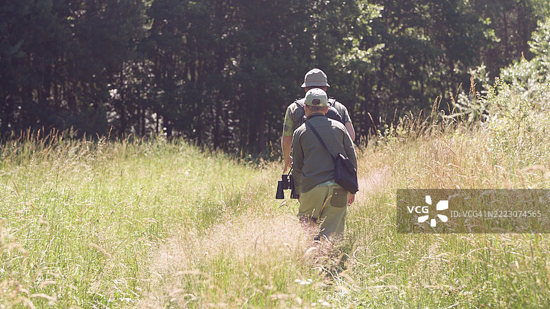 父子一起背包穿越绿意盎然的夏季森林，享受鸟类观察的家庭冒险。图片素材