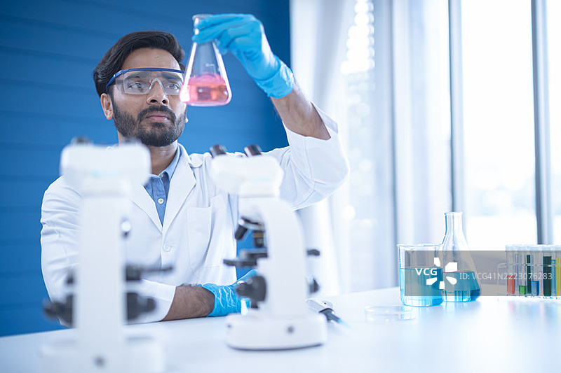 科学家在实验室烧杯中分析溶液，同时使用先进的显微镜，展示现代实验室环境中的创新研究。图片素材