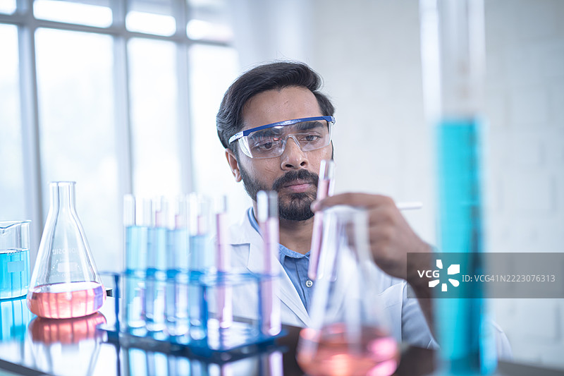 科学家戴着安全眼镜在实验室中检查五颜六色的液体，进行化学研究和分析，以推动科学创新。图片素材