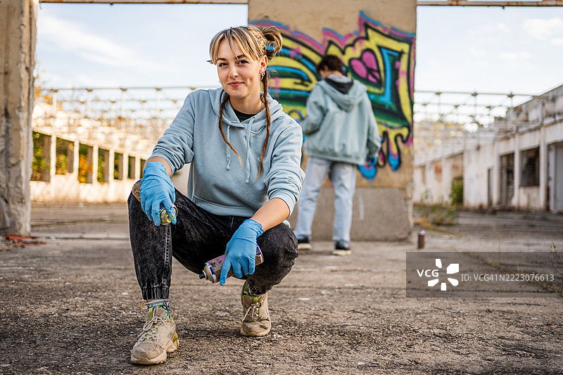 年轻女性涂鸦艺术家在废弃建筑中摆姿势，手持喷漆罐图片素材